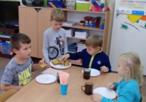 Dyżurny częstuje ciastem dzieci przy stole podczas podwieczorku.